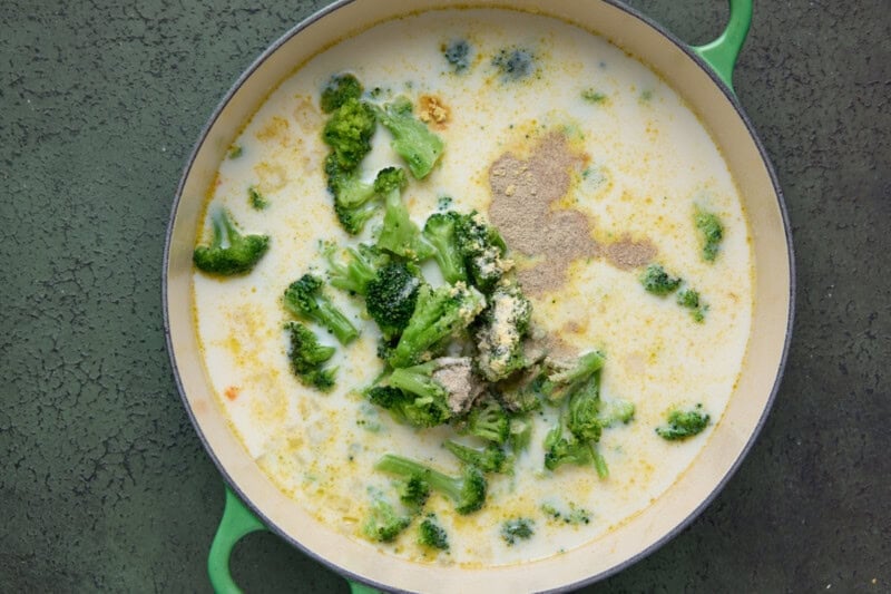 Frozen broccoli being added to soup along with seasonings.