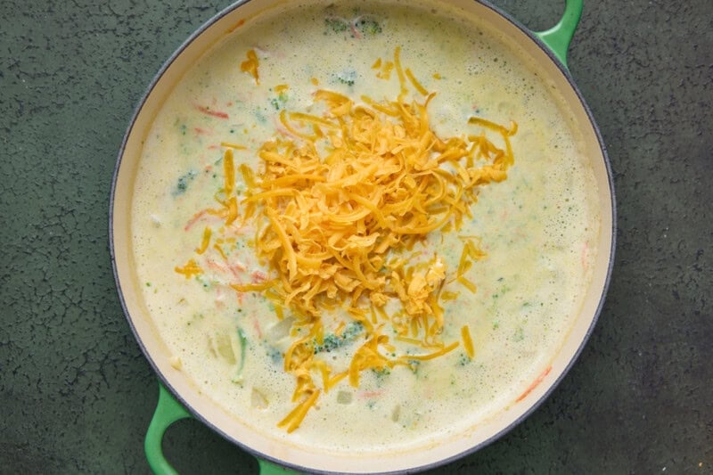 Broccoli soup with grated cheddar cheese on top ready to be stirred in.