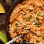 Buffalo Chicken Dip with Blue cheese and green onions with a spoon and celery sticks.