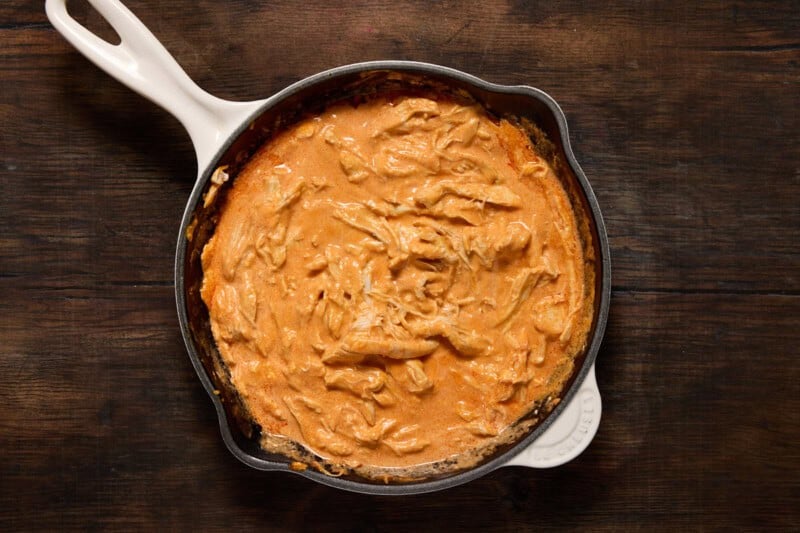 Shredded chicken in cast iron pan with franks red hot sauce and cream cheese stirred in.