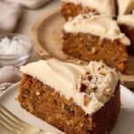 Slice of single layer carrot cake with brown butter cream cheese frosting on a stack of plates along with other slices in the background.