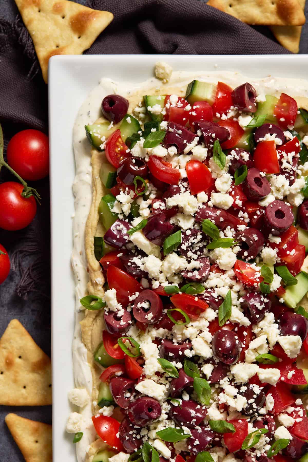 Layered Greek Dip on a white platter with pita chips.
