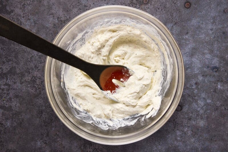 Glass bowl of cream cheese mixed with lemon juice and Italian seasoning.