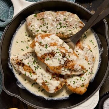 Seared chicken breasts in a skillet with creamy feta cheese sauce.