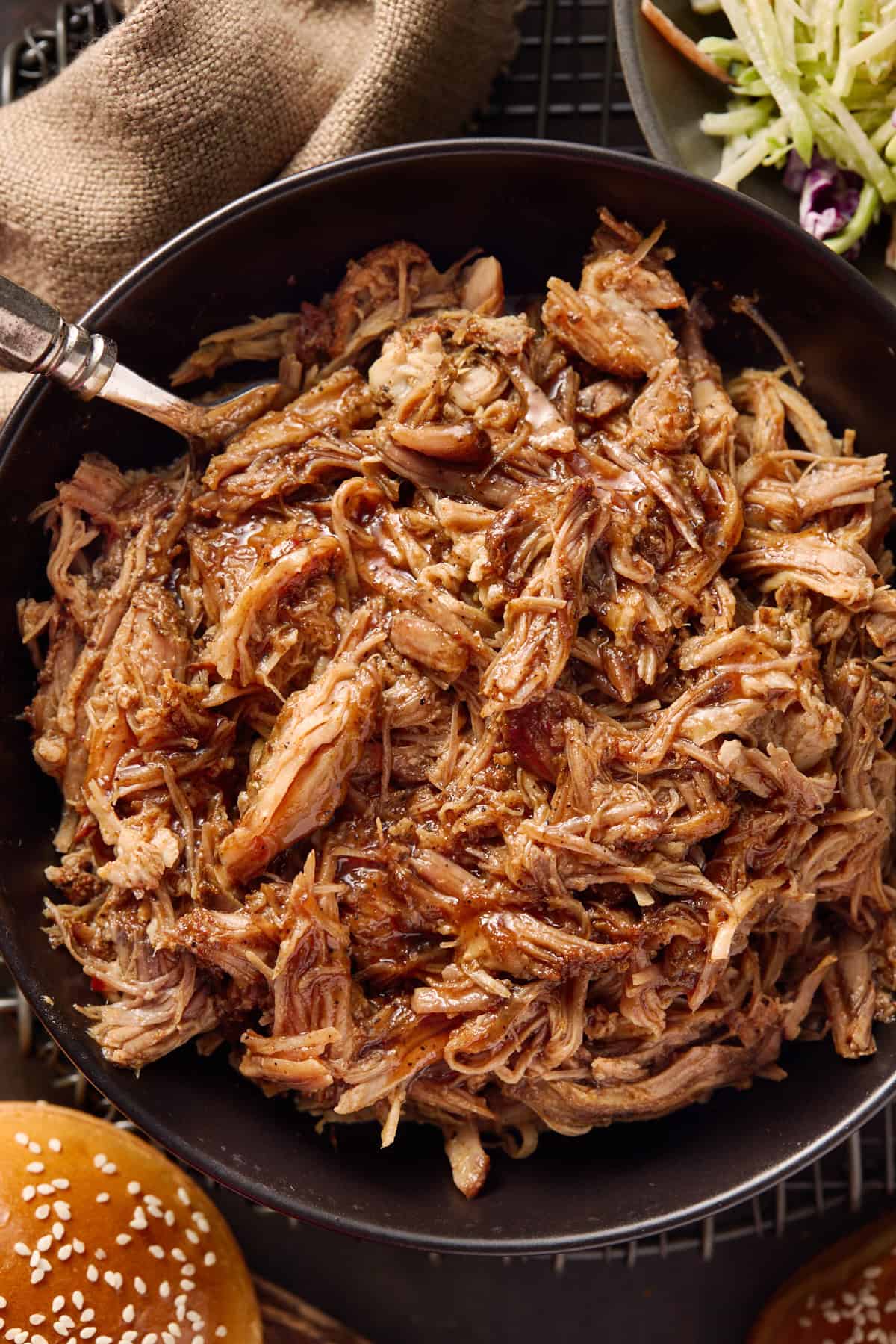 Pulled pork in a bowl with buns and slaw on the side.