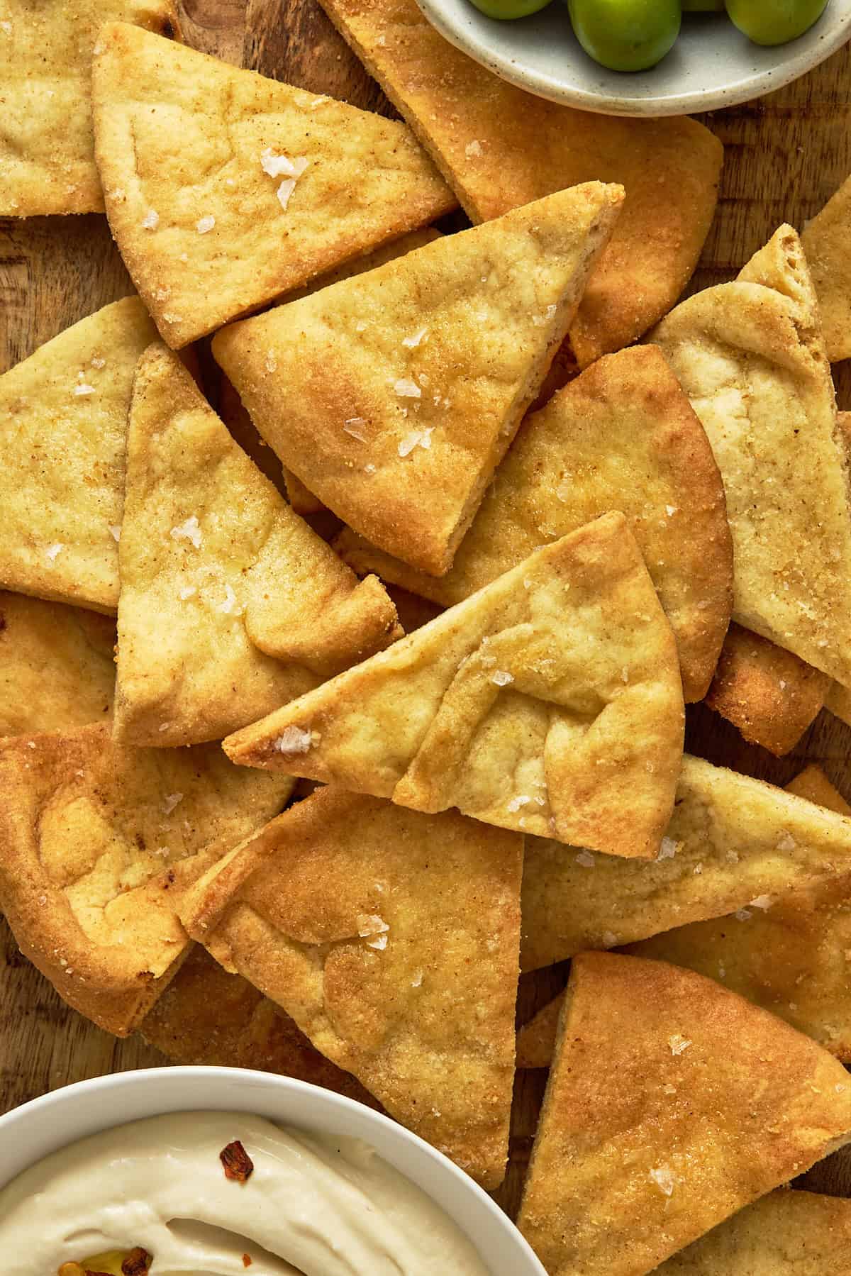 Pile of air fryer pita chips on a wooden board.