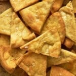 Air fryer pita chips on a wooden board surrounded by a bowl of olives and a bowl of hummus.