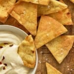 Air fryer pita chips with a bowl of plain hummus on a wooden board.