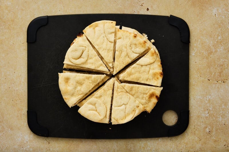 Fresh pitas cut into eighths on a black cutting board.