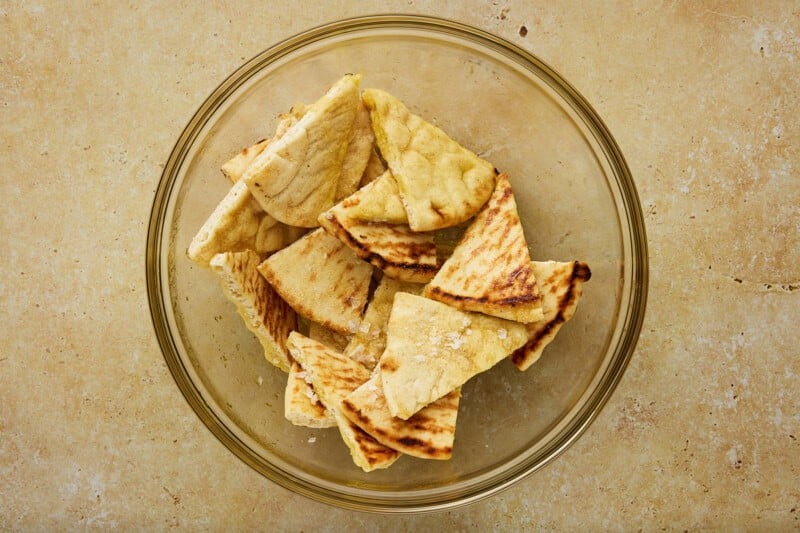 Freshly cut pita chips tossed with oil and salt in a glass bowl.