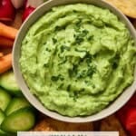 Light gray bowl filled with creamy avocado dip surrounded by fresh crudité and pita chips.