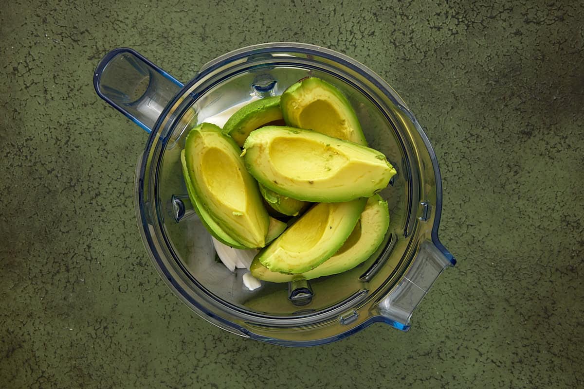Fresh peeled and pitted avocados and other dip ingredients in a blender jar.