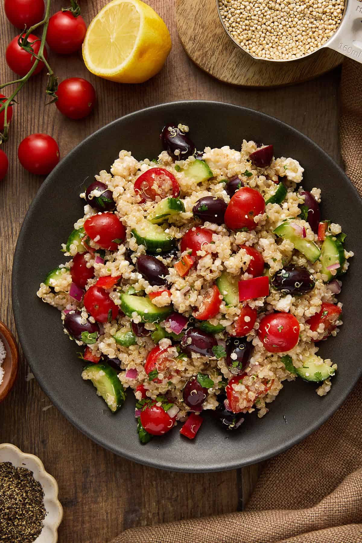 Greek Quinoa Salad on a plate with fresh tomatoes and a half of a lemon.