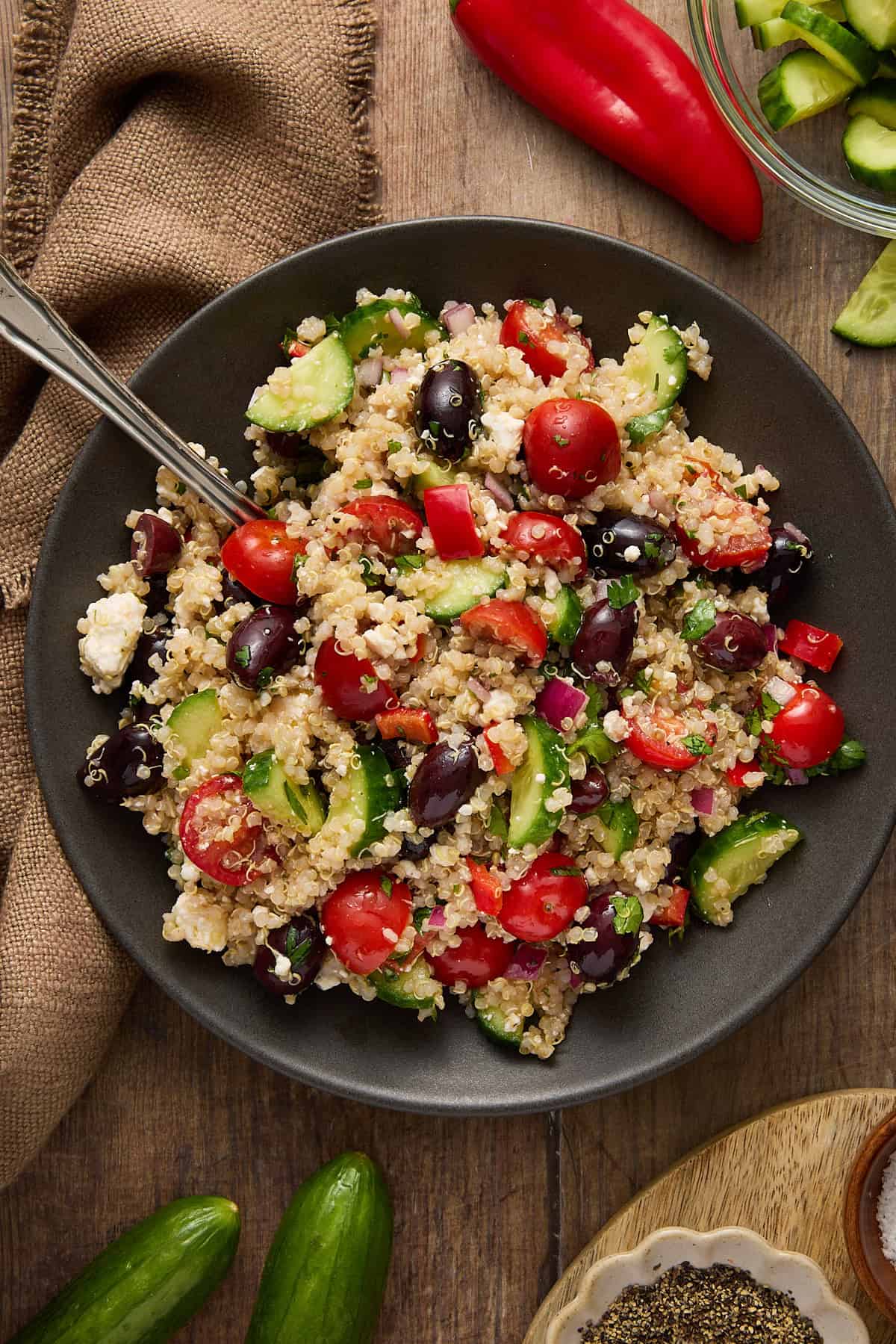 Greek quinoa salad on a plate with a brown napkin and chopped cucumbers on the side.
