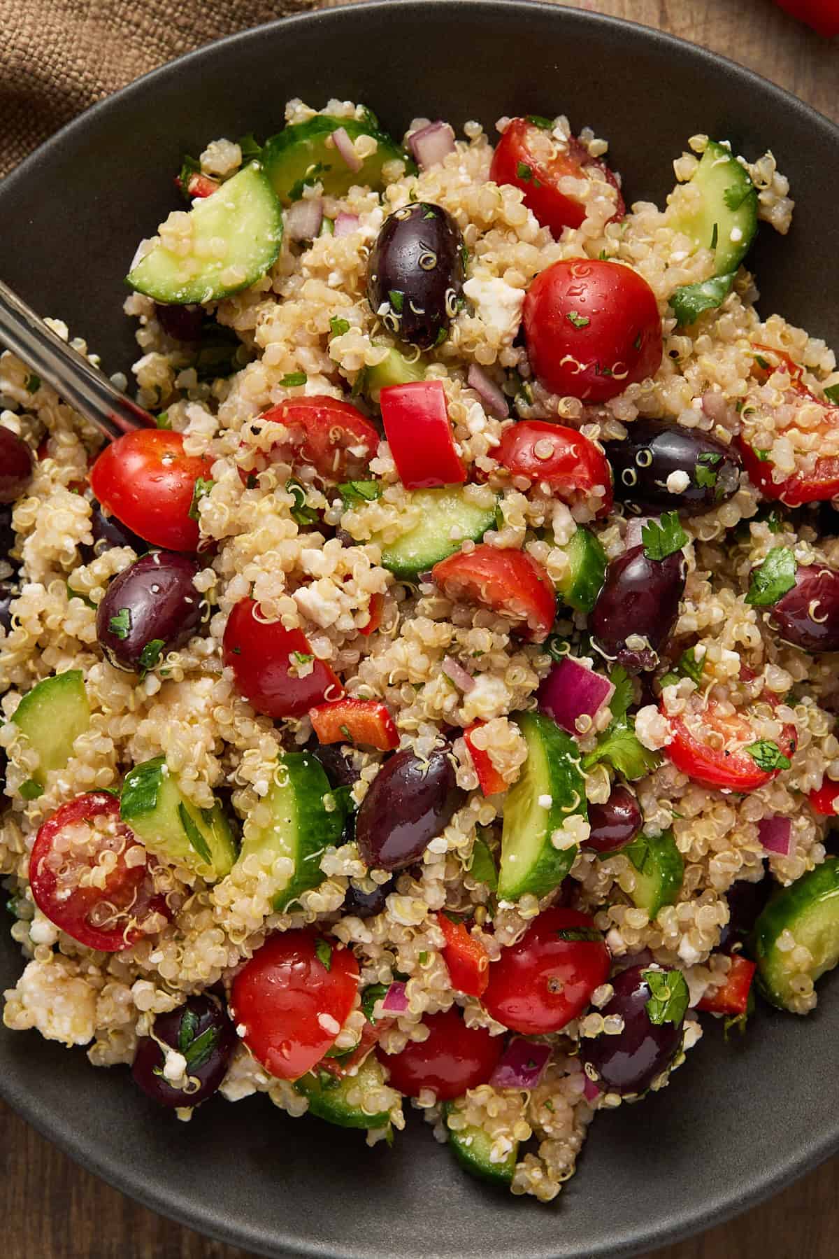 Black plate with greek quinoa salad piled on top with a spoon for serving.