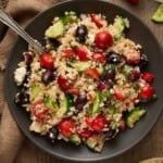 Greek Quinoa salad on a gray plate with cucumbers and peppers.