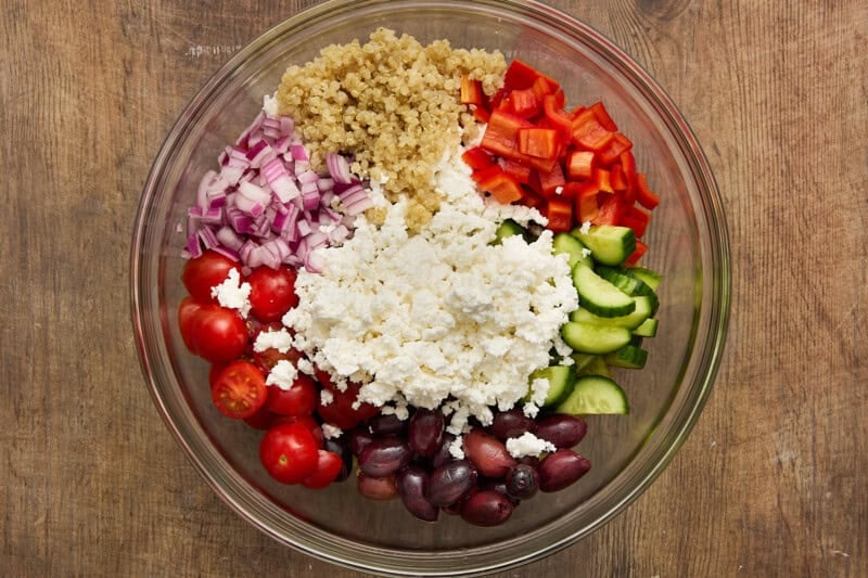 Ingredients needed to make quinoa salad piled in bowl.