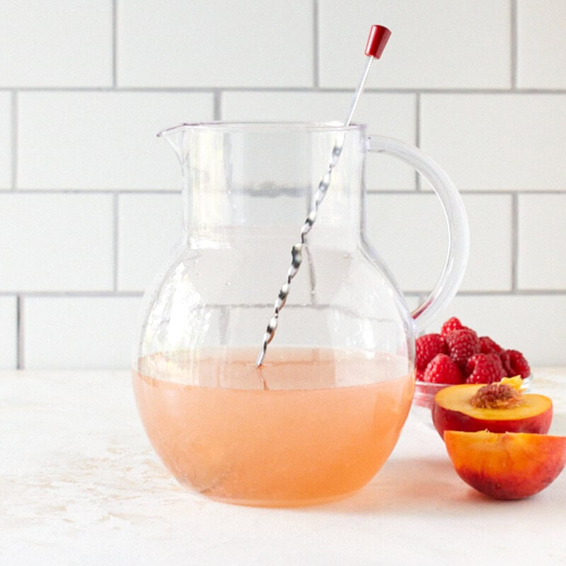 Rosé sangria in a large glass pitcher with a stirring spoon.