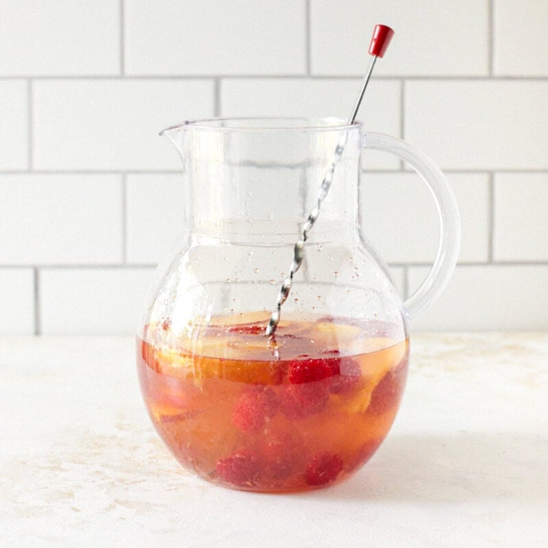 Raspberries and peach slices in glass pitcher filled with rosé sangria.