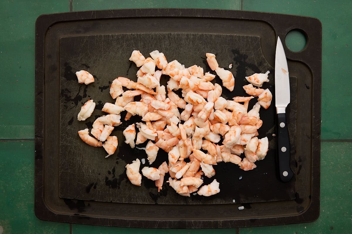 chopped shrimp on a cutting board with a knife.