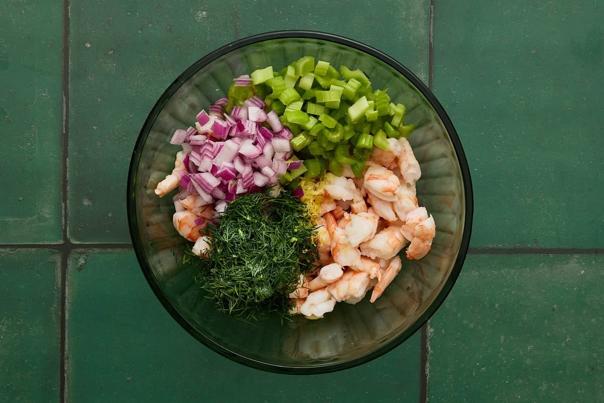 Piles of shrimp, red onion, celery and dill in bowl.