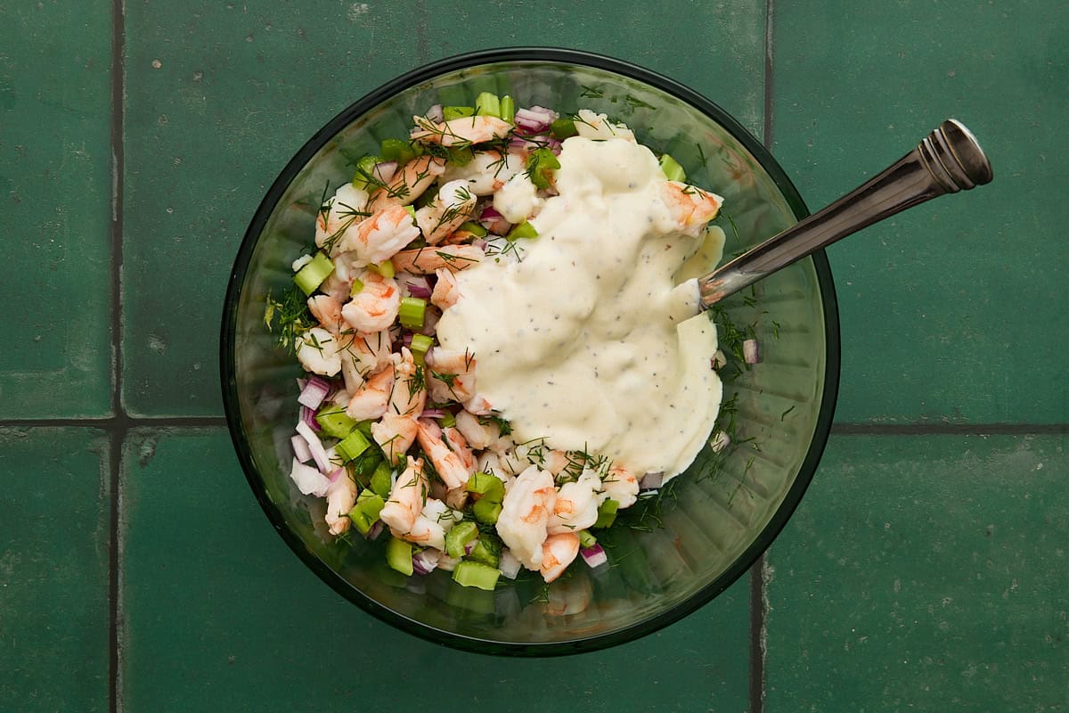 Chopped shrimp. celery and red onion in bowl with creamy dill dressing on top.