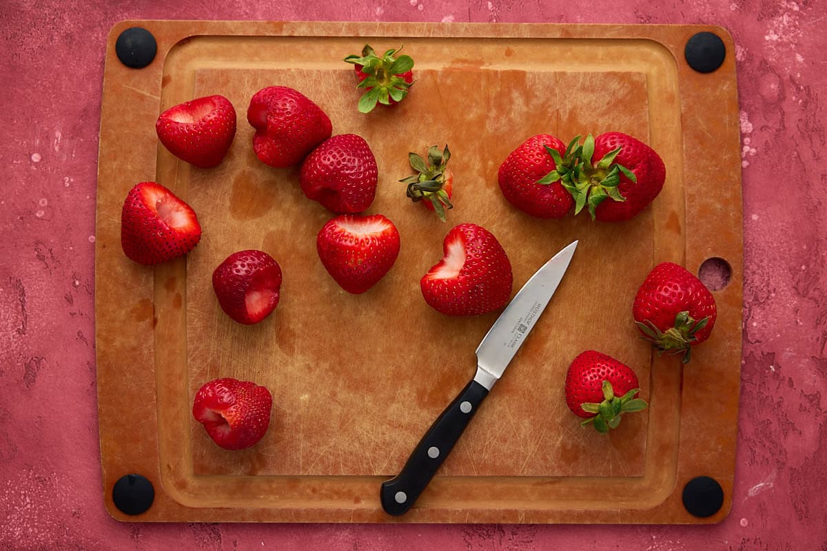 Hulled strawberries and a paring knife on a cutting board.