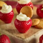 Strawberries stuffed with cheesecake filling and topped with mini Nilla wafers on a wood cutting board.