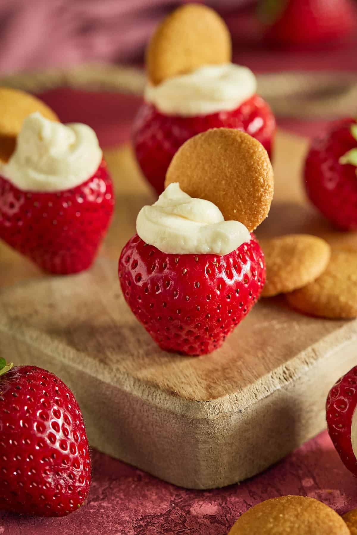 Three strawberries stuffed with cheesecake filling on a wood cutting board.