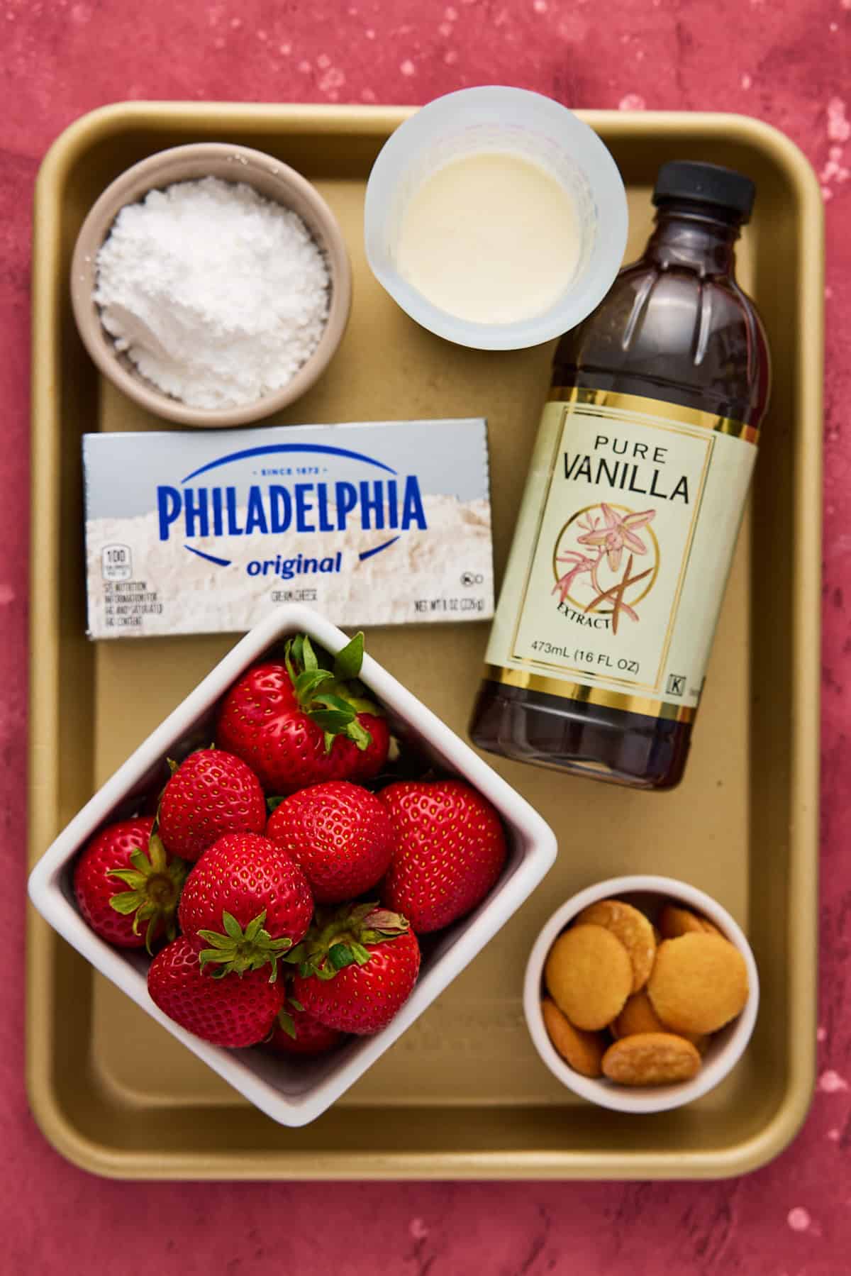 Ingredients on a gold metal sheet pan to make cheesecake stuffed strawberries, including strawberries, cream cheese and heavy cream.