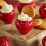 Cheesecake stuffed strawberries topped with a mini Nilla wafter on a wood cutting board.