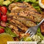 Sliced honey mustard chicken on top of a cobb salad.