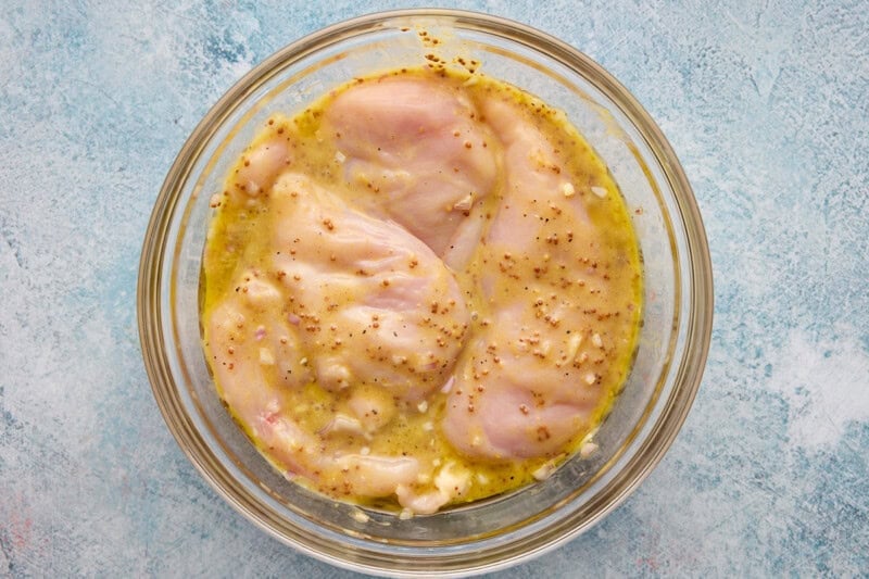 Raw chicken breasts immersed in honey mustard marinade.