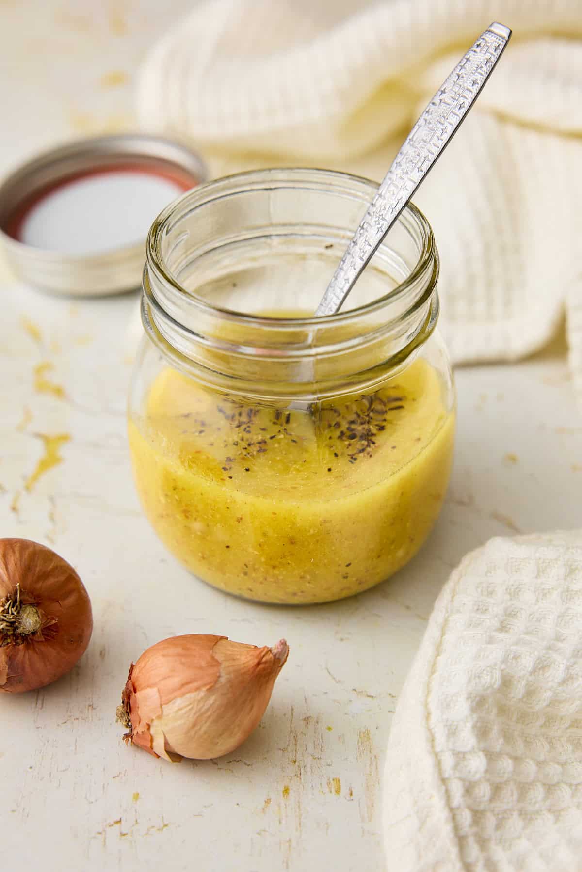 Dijon vinaigrette in a small jar with a spoon and fresh cracked pepper on top.