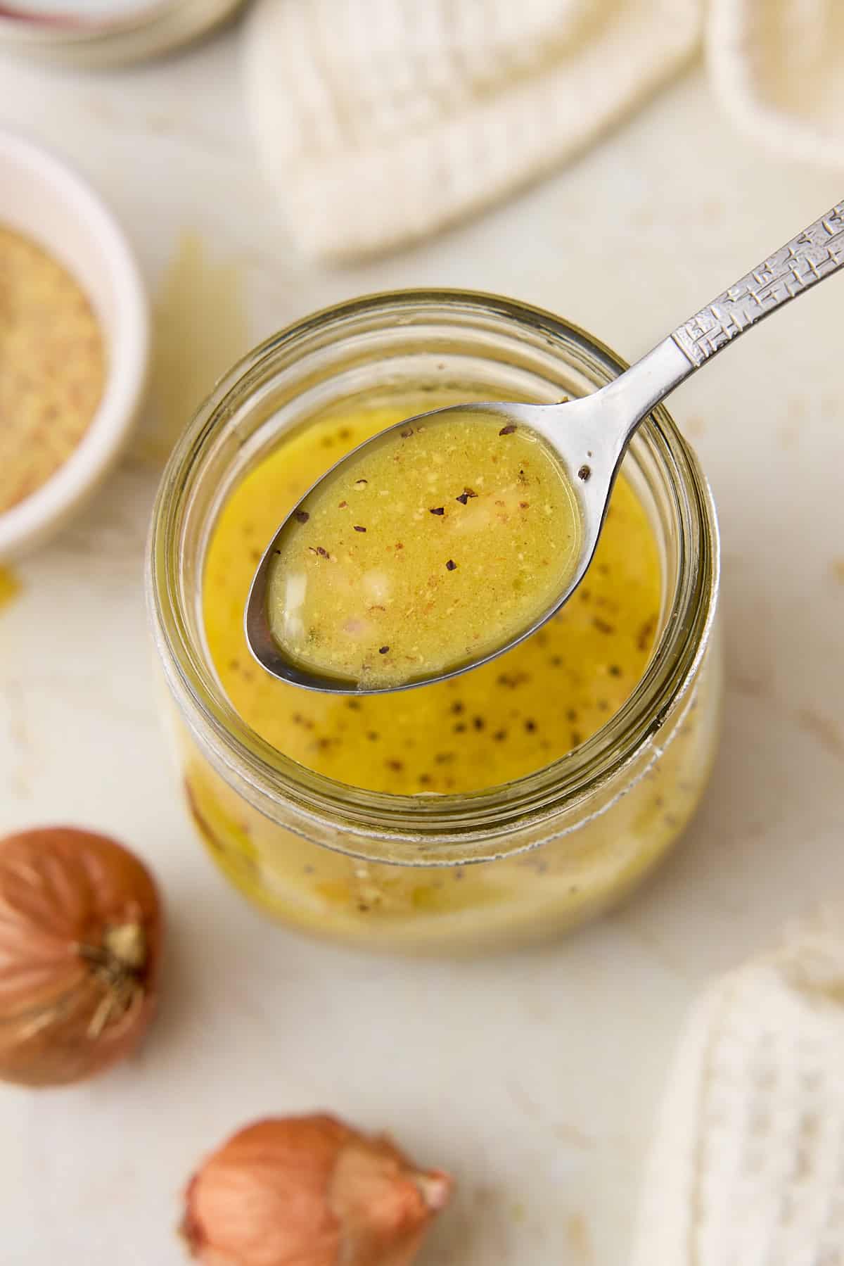 A spoonful of dijon mustard vinaigrette over a jar.