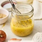 A small glass jar filled with Dijon Vinaigrette and a whisk.