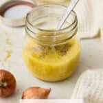 A small glass jar filled with Dijon Vinaigrette and a small spoon.