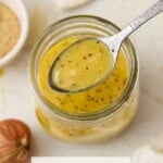 A spoonful of Dijon Vinaigrette over a glass jar with a white linen.