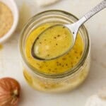A spoonful of Dijon Vinaigrette over a small glass har with mustard and shallots on side.