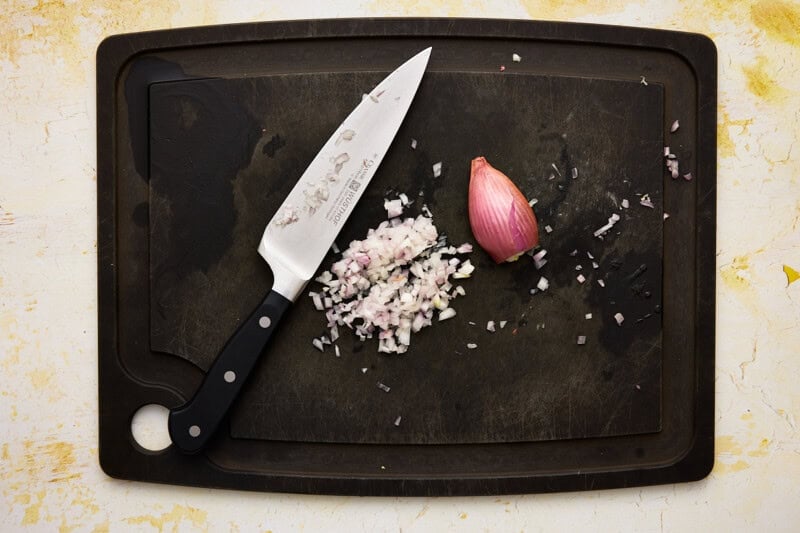 Shallots minced on a black cutting board with a knife.