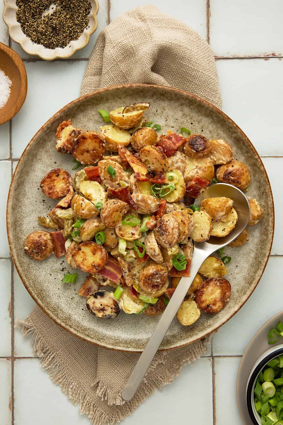 A speckled beige ceramic plate with grilled potato salad and a silver serving spoon.