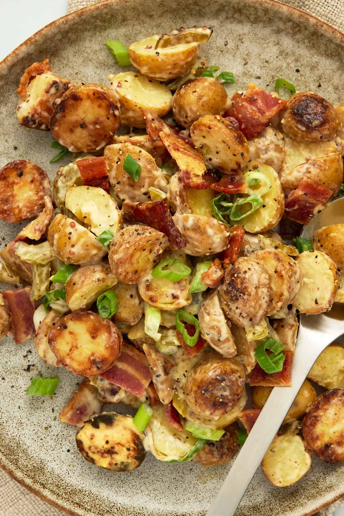 A speckled ceramic plate piled high with grilled potato salad and a serving spoon.