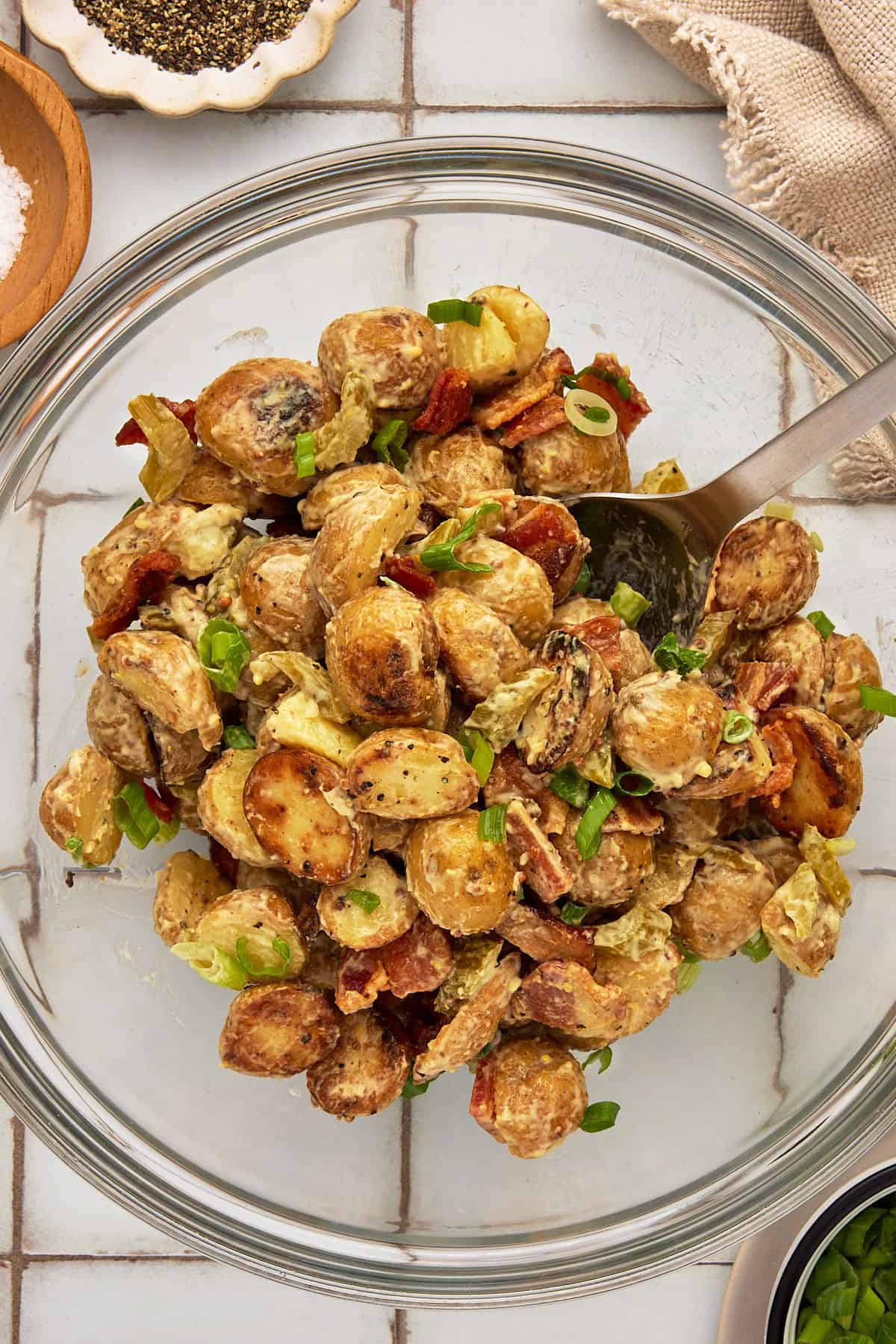 A glass bowl filled with Grilled Potato Salad with Bacon and a silver serving spoon.