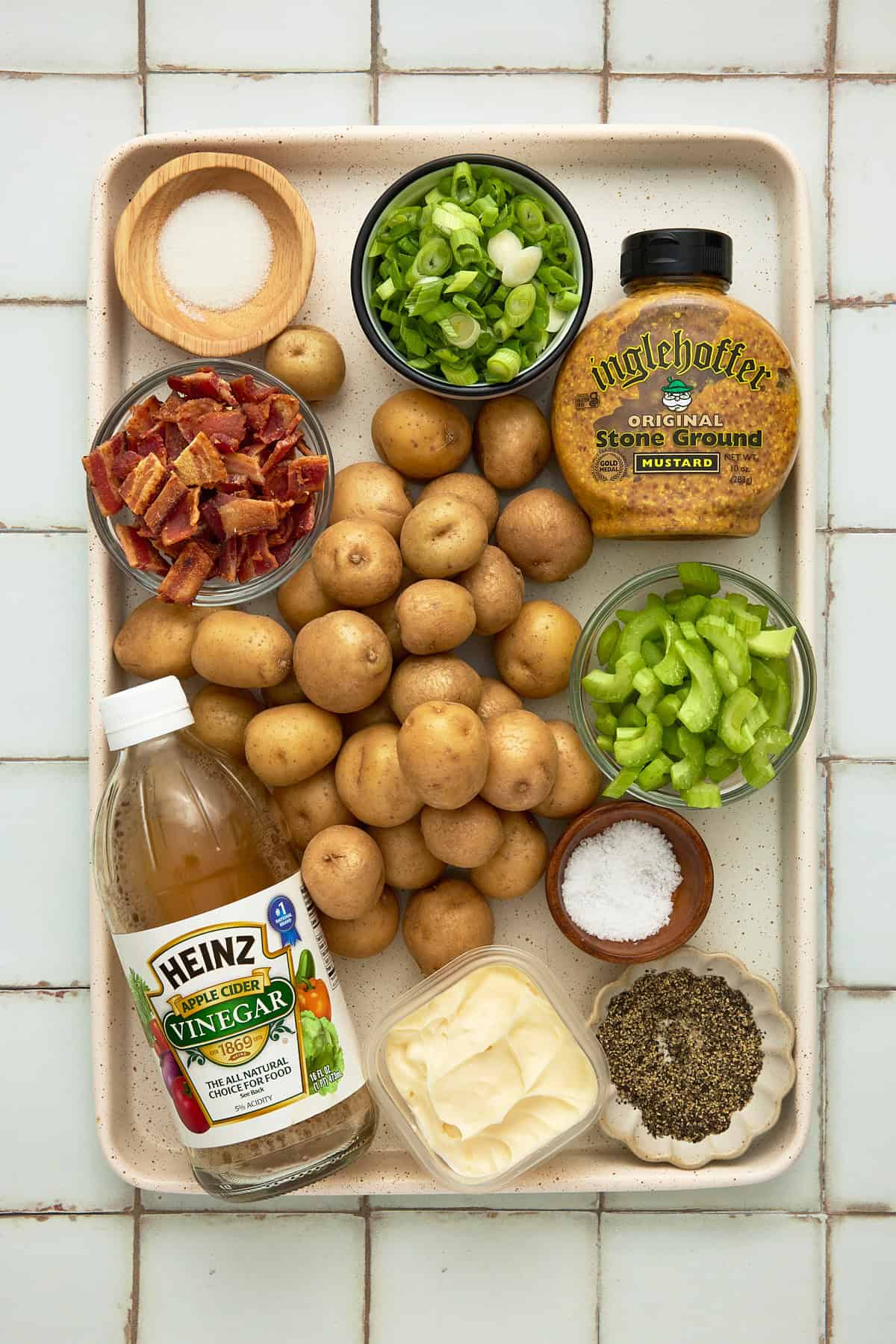 A cream sheet pan filled with ingredients to make Grilled Potato Salad with Bacon including baby potatoes, mustard, bacon and celery.