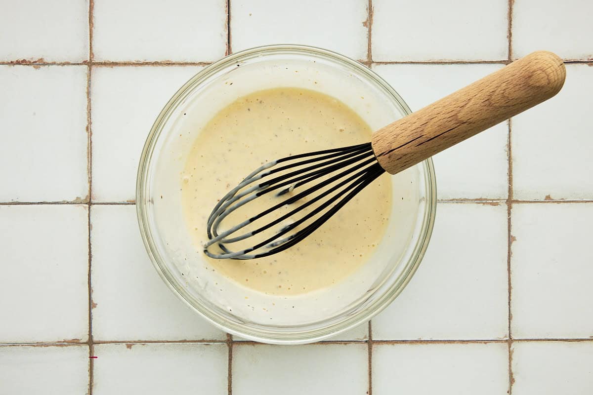 Grilled Potato Salad dressing mixed together in a glass bowl with a whisk.