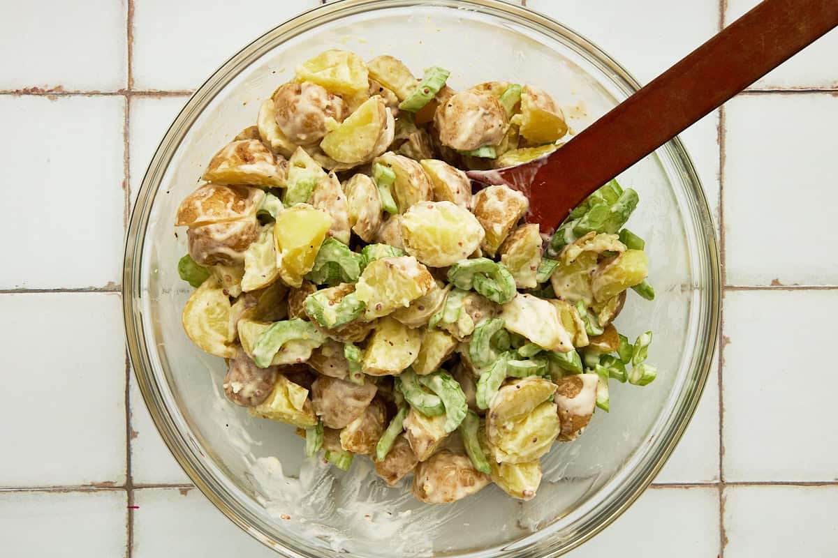 Parboiled potatoes, celery and potato salad dressing mixed together in a glass bowl.