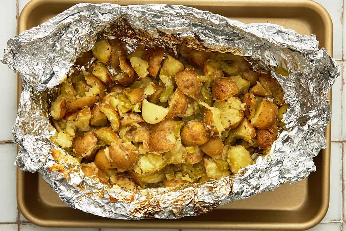 A foil packet of grilled potatoes on a gold sheet pan.