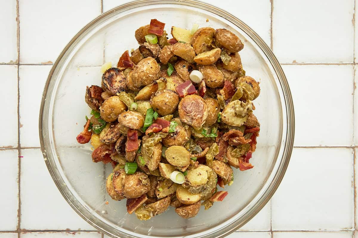 A glass bowl filled with grilled potato salad with bacon and green onions.