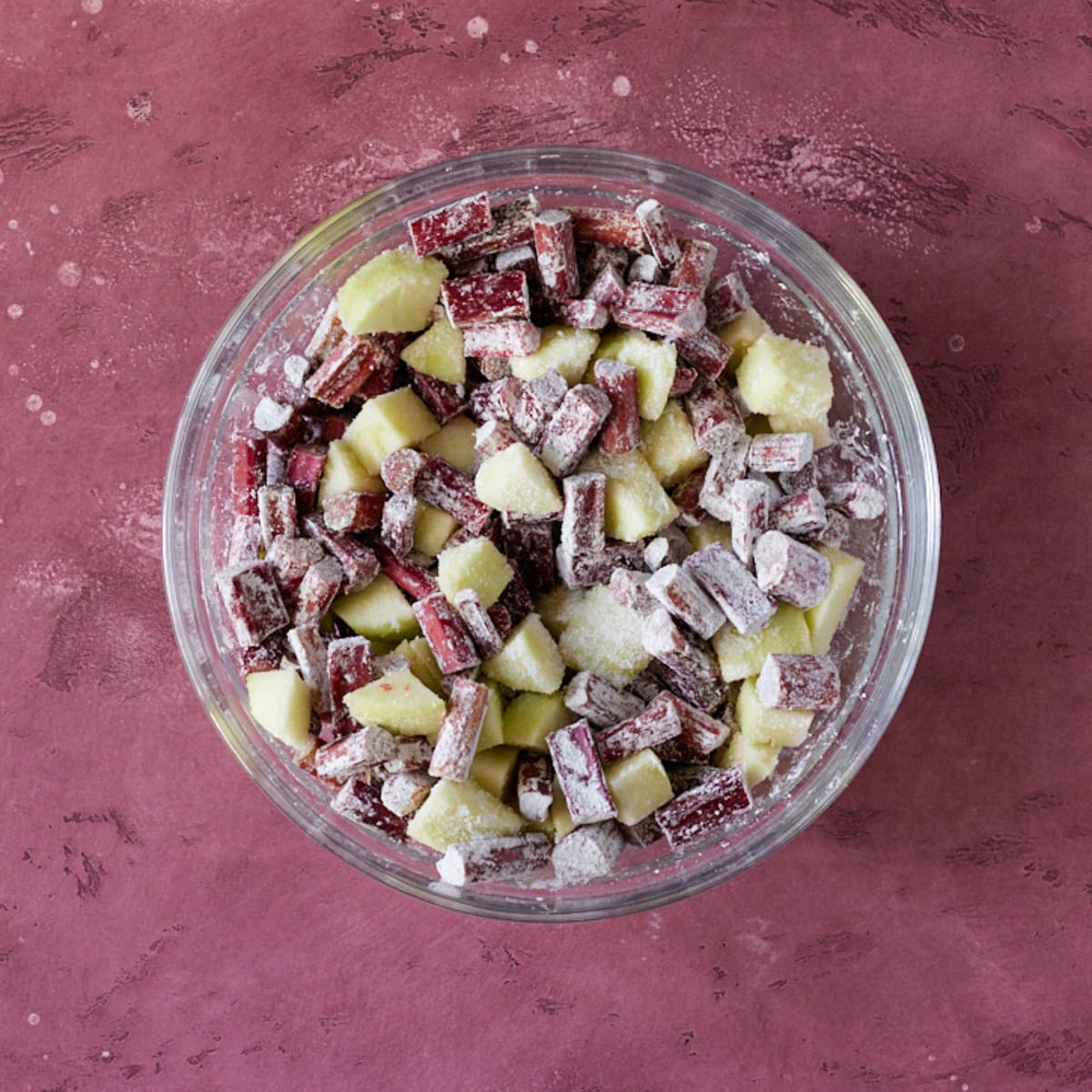 Rhubarb and apples tossed with sugar and corn starch in glass bowl.