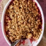Apple Rhubarb Crisp in an oval baking dish with a spoonful out and a spoon for serving.